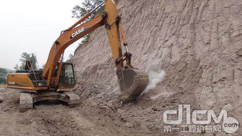 凯斯CX240B液压挖掘机正在采挖砂岩，坚硬的岩石被刮削的冒出了阵阵浓烟