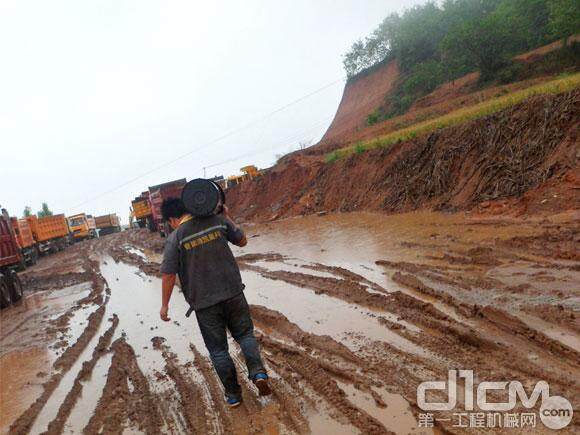 服务工程师肩扛近20公斤的液压油冒雨行走在通往工地的泥泞山路上