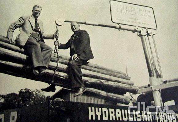 图中着深色服装的为希尔博创始人Eric Sundin先生，他右手边的同伴是Einar Frisk先生。他们正在演示HIAB 19型——世界上第一台随车起重机。