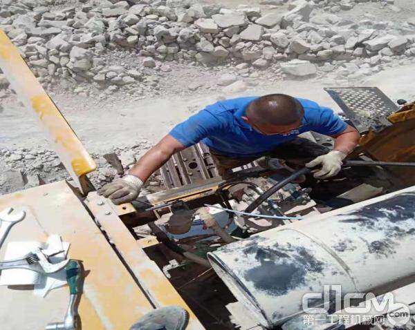服务工程师孙猛，正在在矿山修理车辆，他的身后就是一个小的断崖 